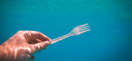 Hand under water holding a white plastic fork