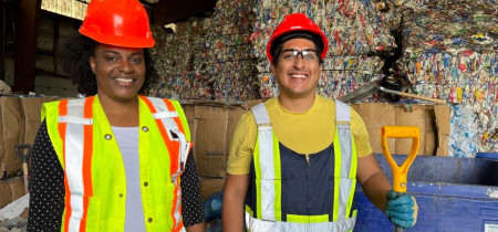 2 people smiling infront of recycling