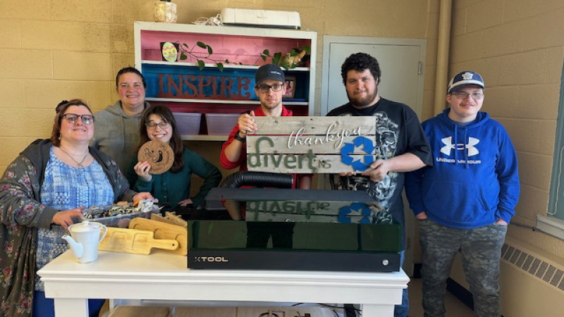 people standing around a table holding a wooden sign that says thank you divert ns