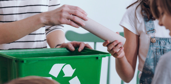 a childs hand holding an empty paper towel holder handing it to a person to recycle