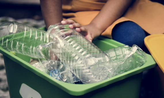 a hand placing an empty bottle into a recycling bin