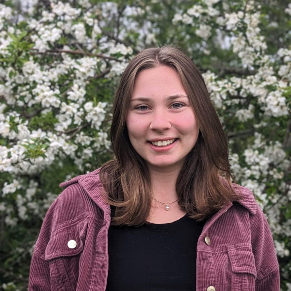 girl in purple jacket standing in front of flowers 