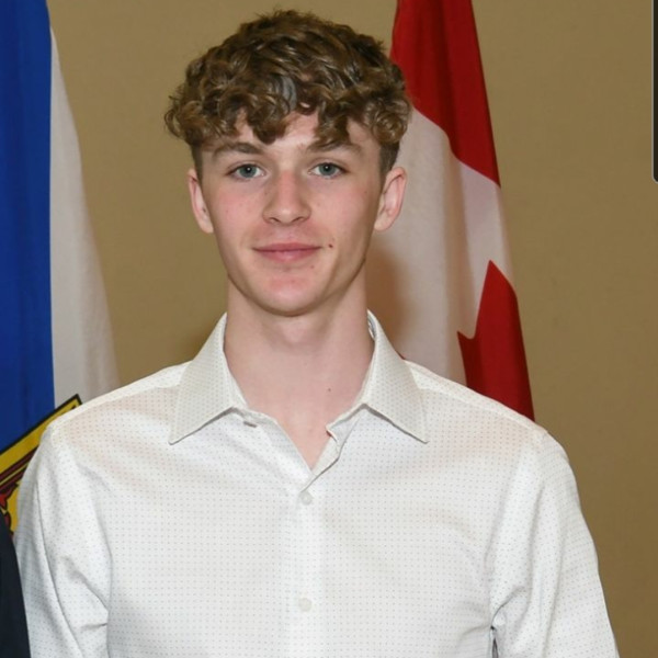 Jake Feener in a white button up dress shirt in front of the Nova Scotia and Canada flags